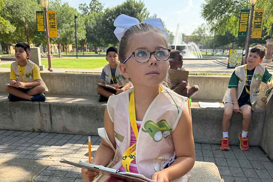 A young girl with a clipboard looking up into the trees for birds