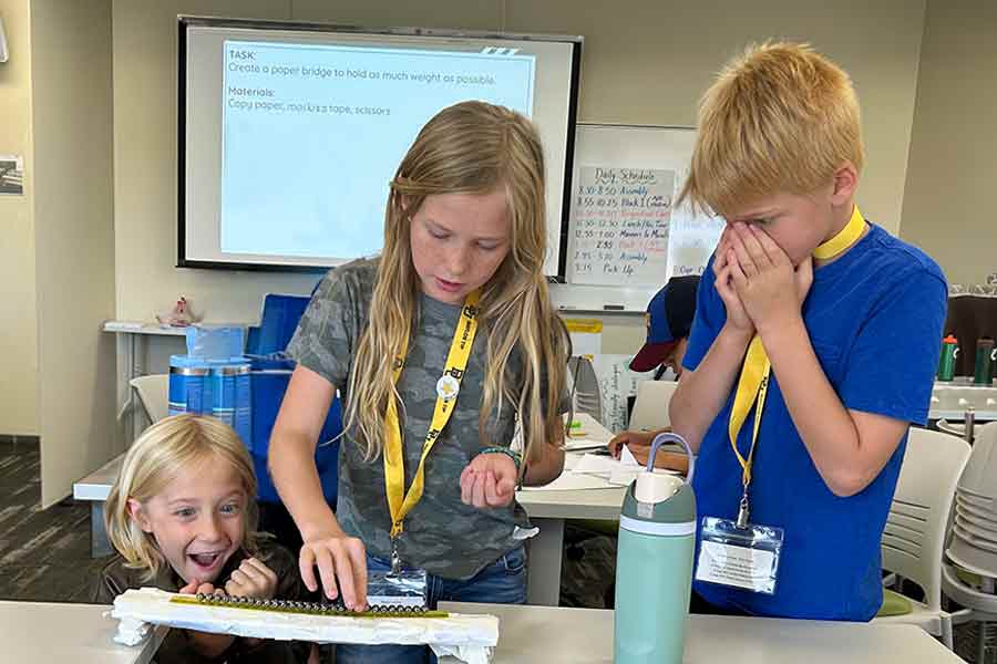 Three boys experimenting with how much weight their bridge can hold