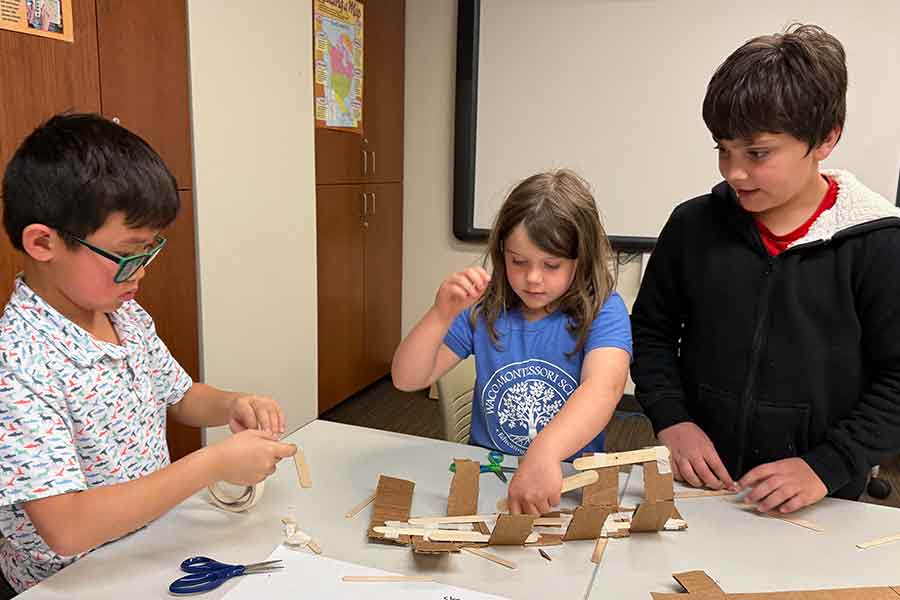 Three young children building a bridge together out of cardboard and tape