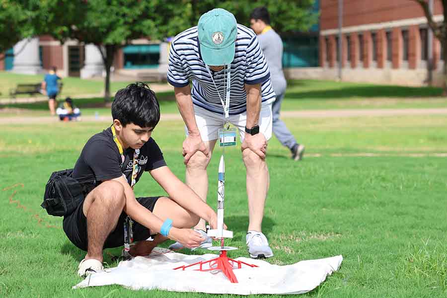 A high school boy and an instructor in a field getting a rocket ready to launch