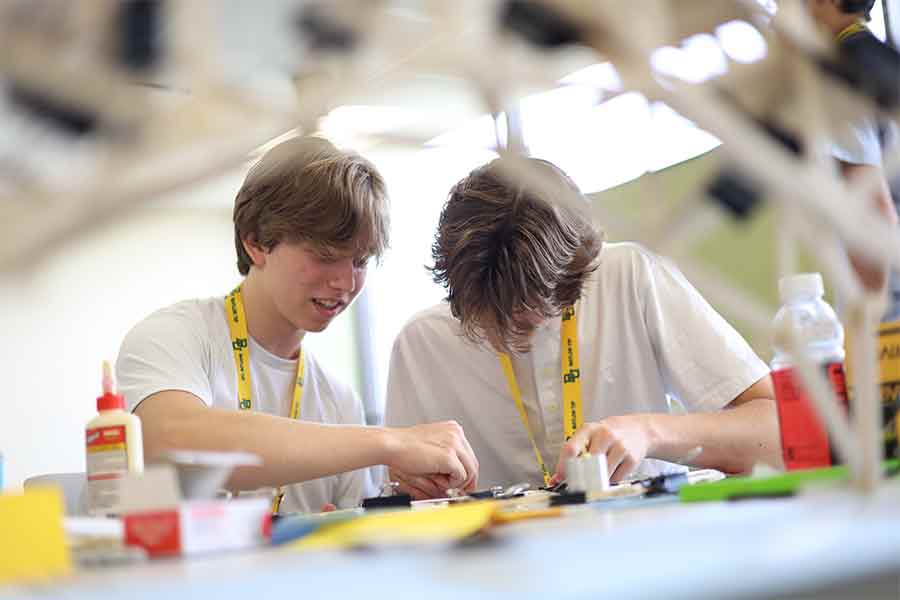 Two high school boys building a balsa wood bridge together at a table in TIP Academy summer programming