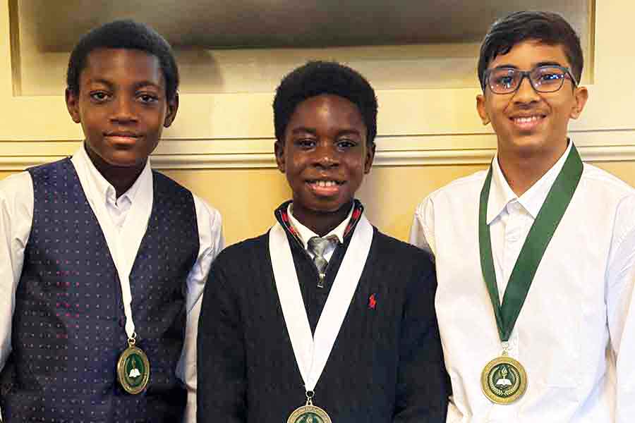 Three 7th grade boys at with medals around their necks at the 7th grade recognition ceremony
