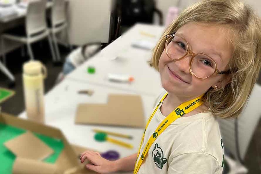 middle grades girl with blonde hair and glasses looking over her shoulder at the camera