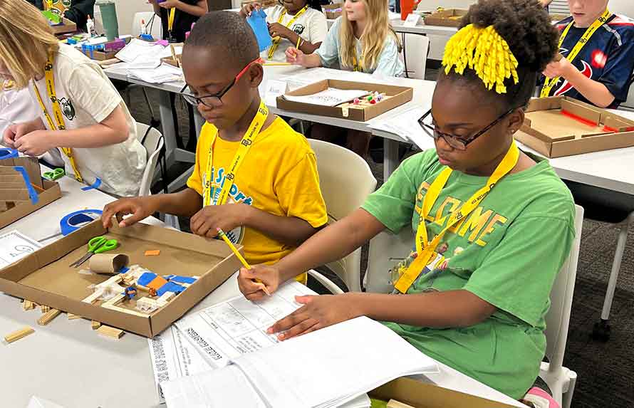 Two middle grades students writing rules and building a game board at a table in the Tabletop Games course