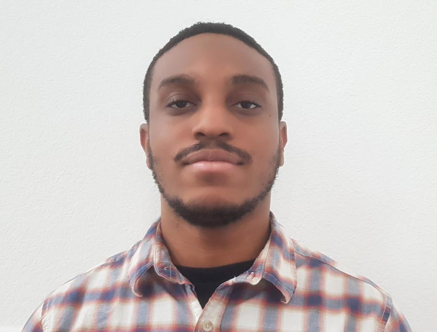 Andi staring at the camera in front of a white background. He has a slight smile and is wearing a plaid shirt. 