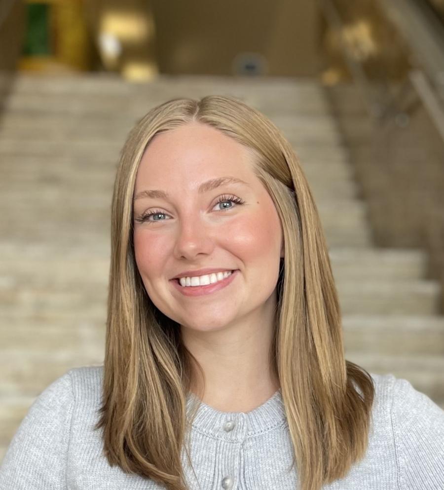 Lauren in a grey cardigan with blonde hair hitting her shoulders. She is smiling widely at the camera. 