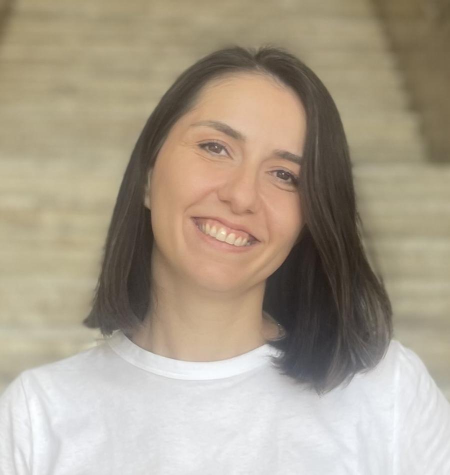 Nilay smiling at the camera in front of some stairs. She has short dark hair and is wearing a white t-shirt. 